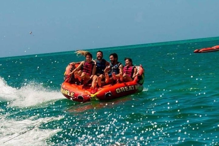 Two men and two women on a large tube being pulled by a boat which is out of the frame